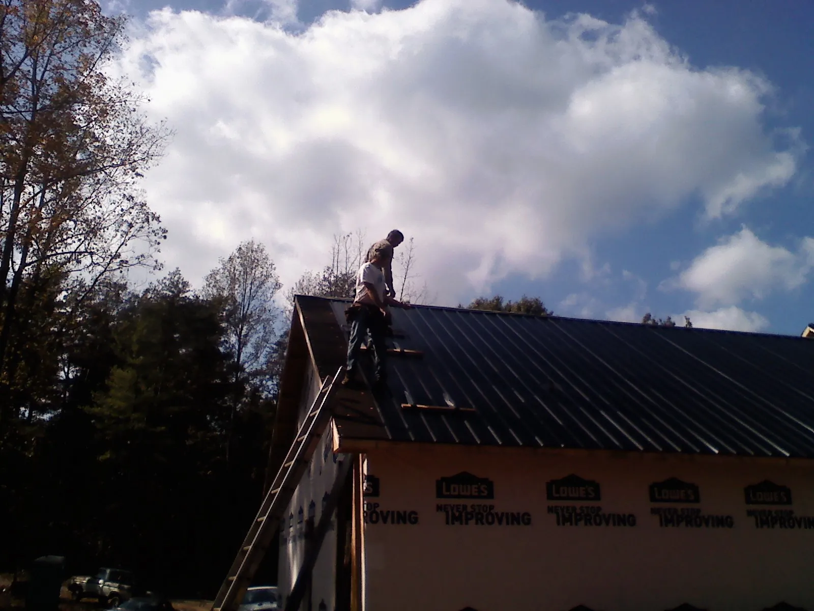 Roofer fastening dark metal panels high against a cloudy sky, from a Roof Inspection job in East Hampton