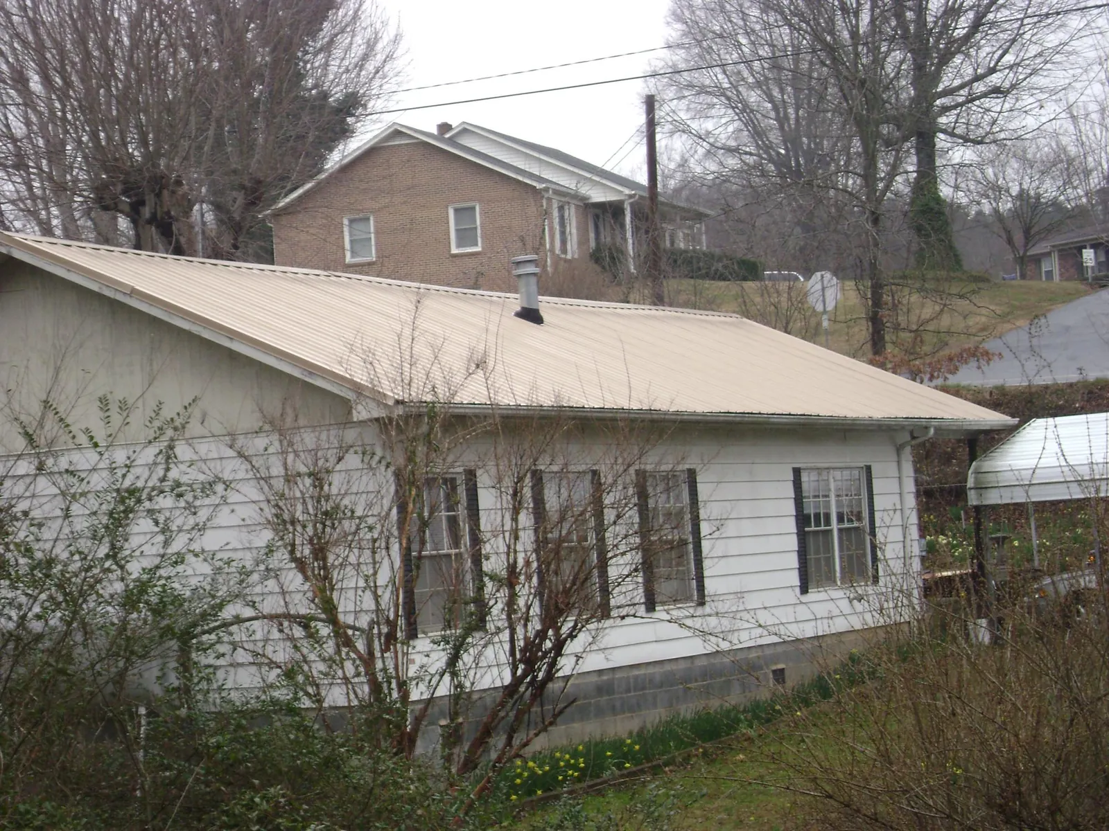 Tan metal roof on a white sided house set into a hillside — Commercial Roofing by Roofing Brothers in East Hampton